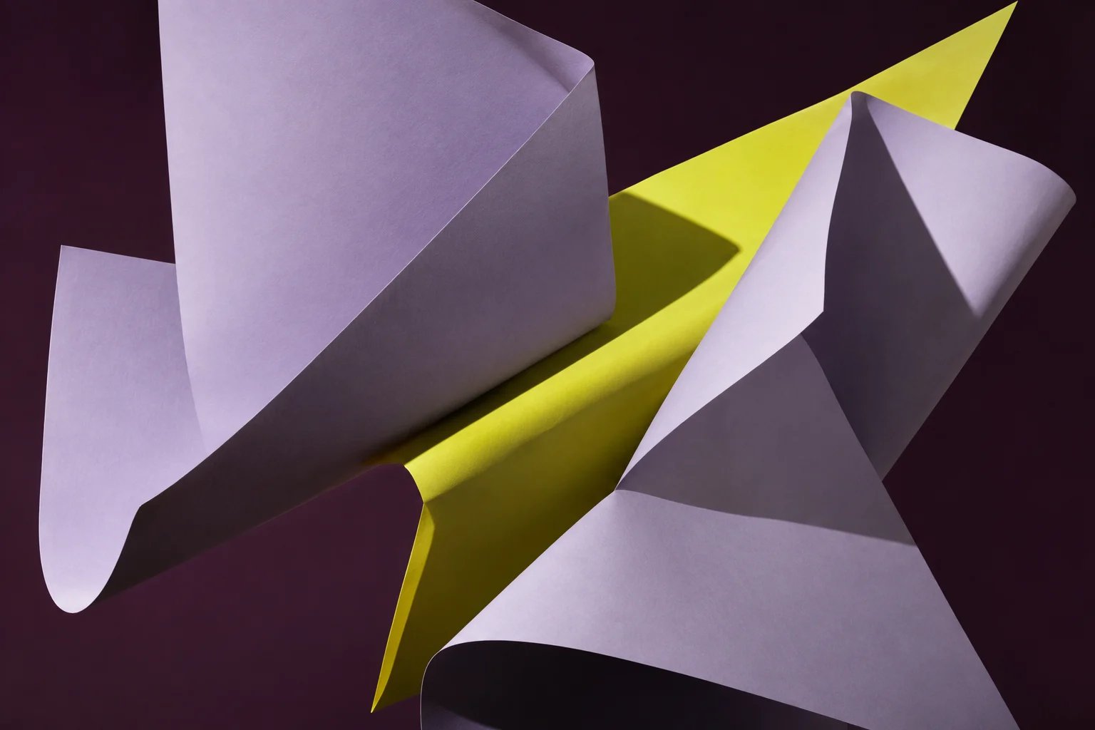 Lavender paper sculpture with an acid-yellow fold against a dark studio backdrop
