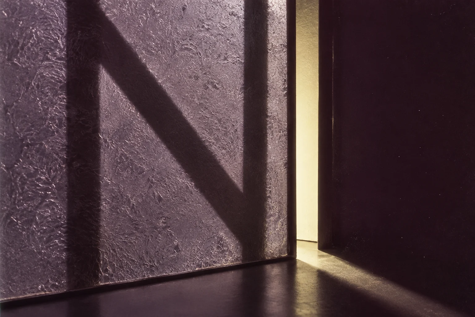 Angular shadows and a pale slit of light through textured lavender glass